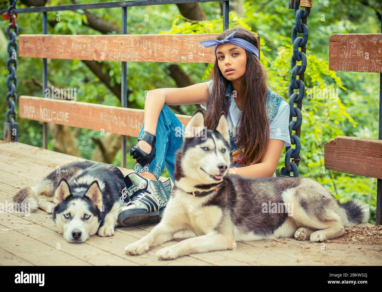 Pretty girl and her pets. Swag rapper woman with her husky dogs isolated  green park background sitting on bridge all three looking at you camera. Tak  Stock Photo - Alamy