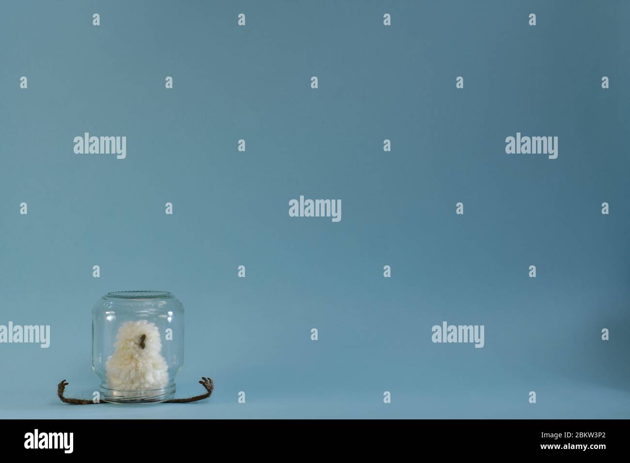 A toy chick of a chicken sits in isolation, legs are stretched to the sides under a transparent jar. Stock Photo
