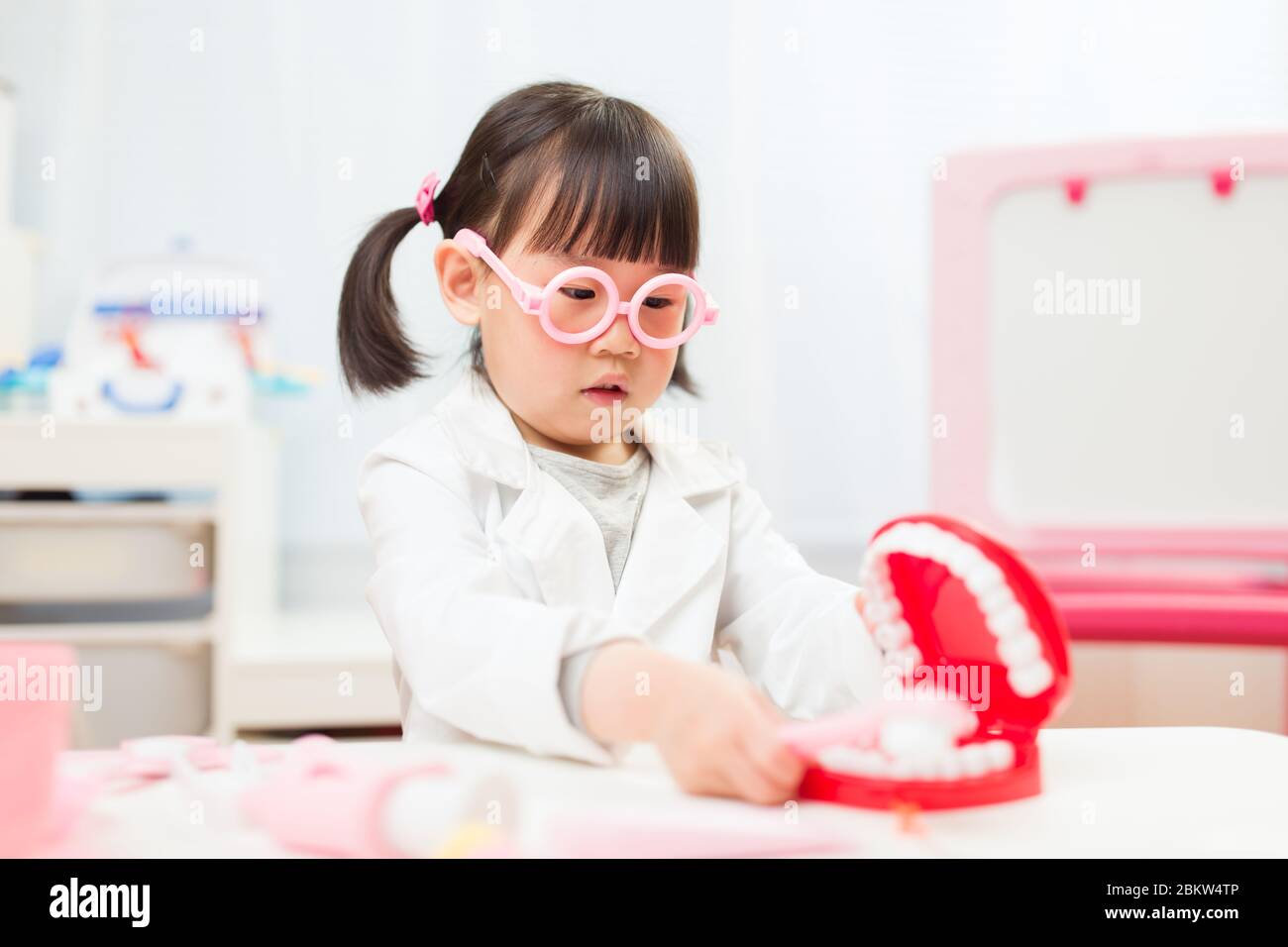 toddler girl pretend play dentist role at home against white background