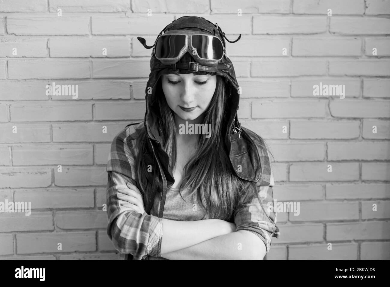 Portrait of a girl in a pilot's cap and glasses on a brick wall background, black and white photo Stock Photo