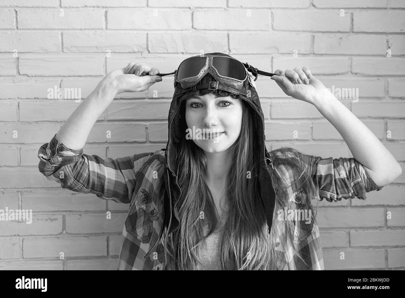 Portrait of a girl in a pilot's cap and glasses on a brick wall background, black and white photo Stock Photo