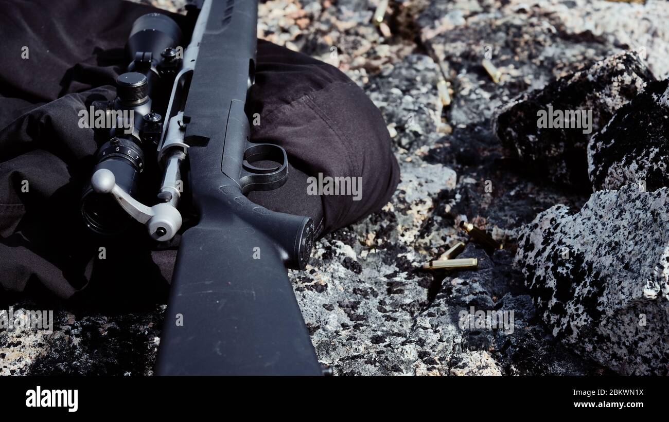 .223 or 5.56MM, empty rifle bullet shell on soil with bolt action rifle lying on the ground besides Stock Photo