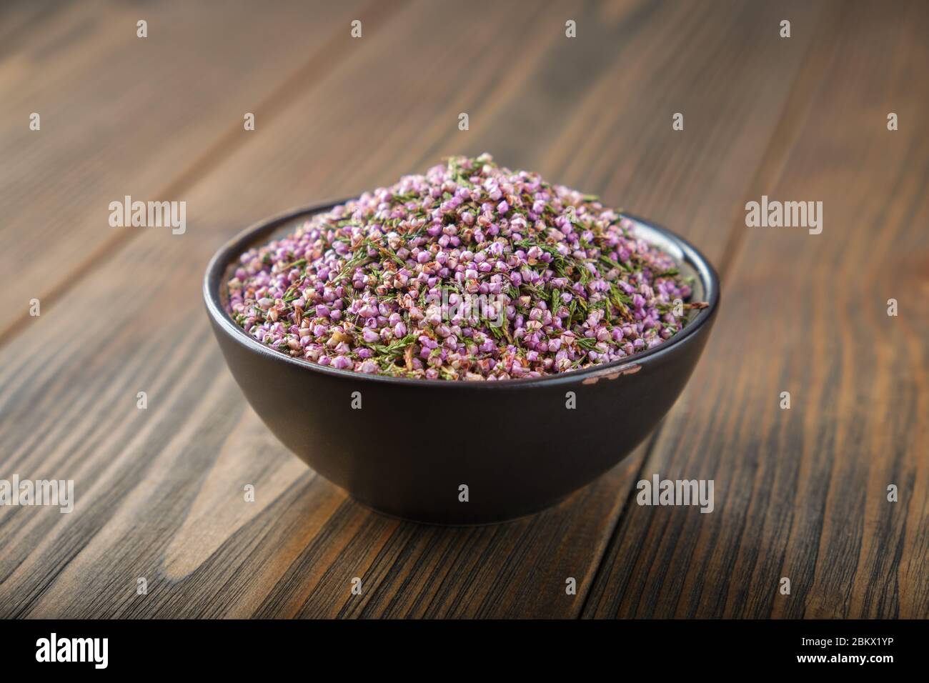 Black bowl of dry healthy heather flowers on wooden table. Stock Photo