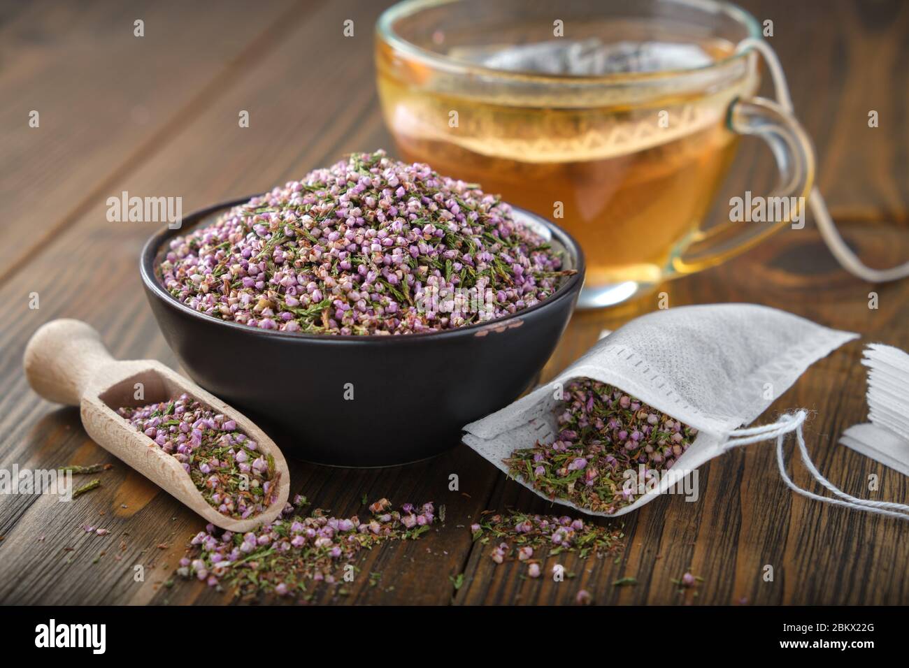 Bowl of dry healthy heather, tea bag with Еrica flowers. Glass tea cup with herbal teabag inside on wooden table. Herbal medicine. Stock Photo