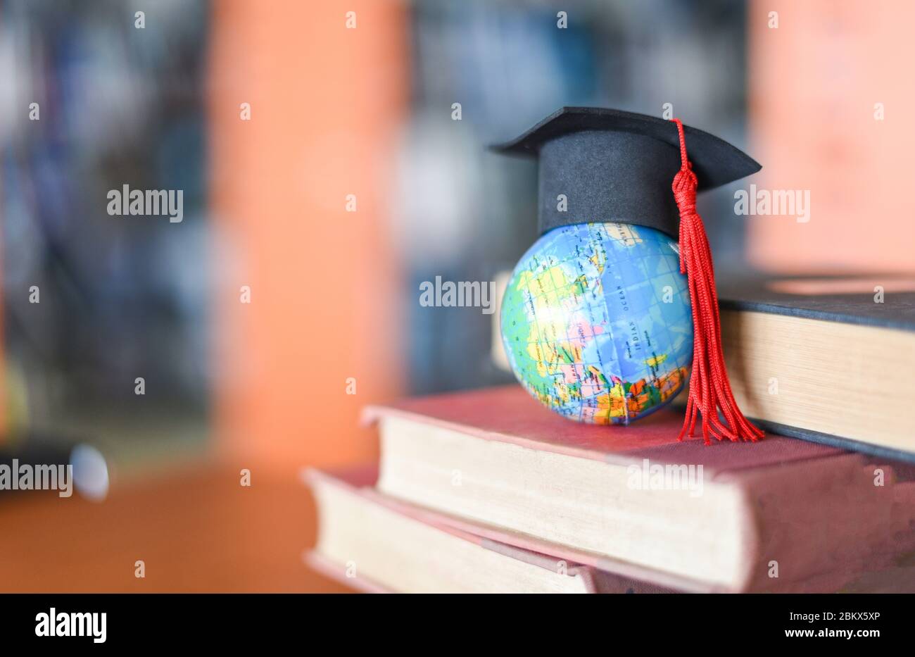 Books on the table in the library / Education learning old book stack and graduation cap on earth globe model on wood desk and blurred bookshelf room Stock Photo