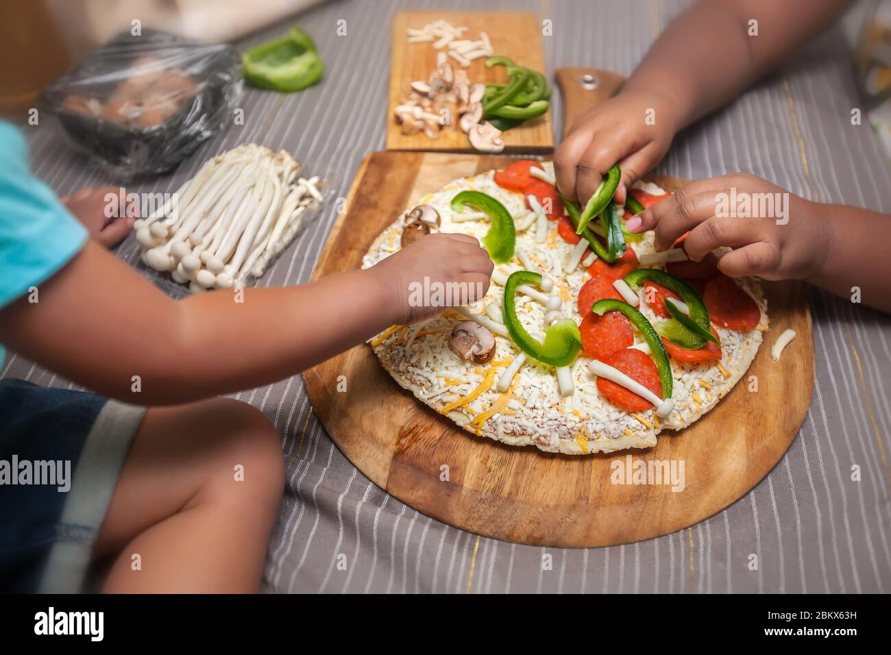 Children adding fresh toppings to a frozen cheese pizza on a wooden