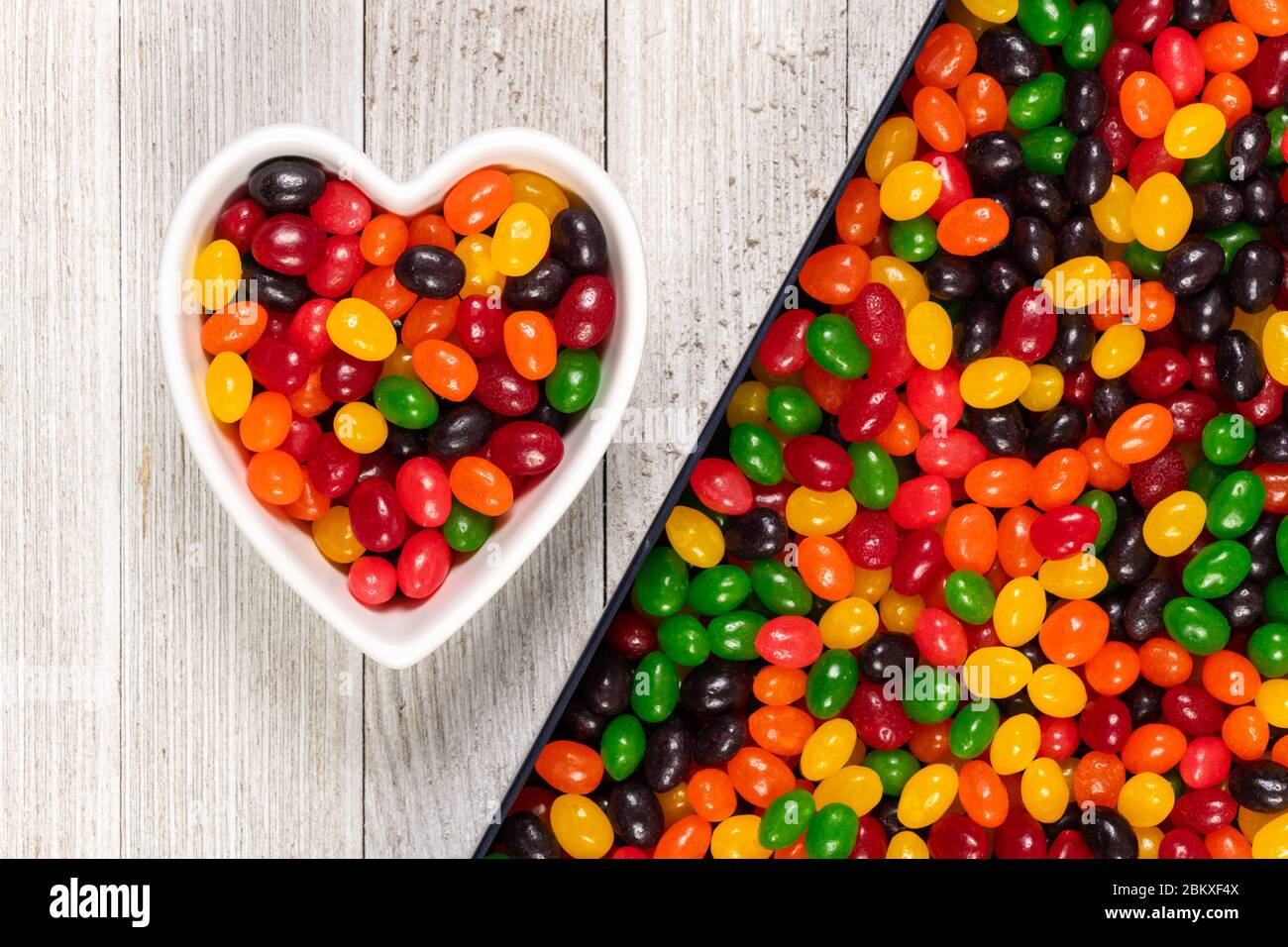 Assorted colorful black, red, green, yellow, and orange jelly beans, sweet candy background with a heart-shaped bowl. Kids' junk food. Stock Photo