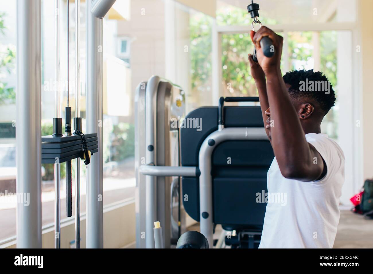 Strong African American man in sportswear pulling cable with bar