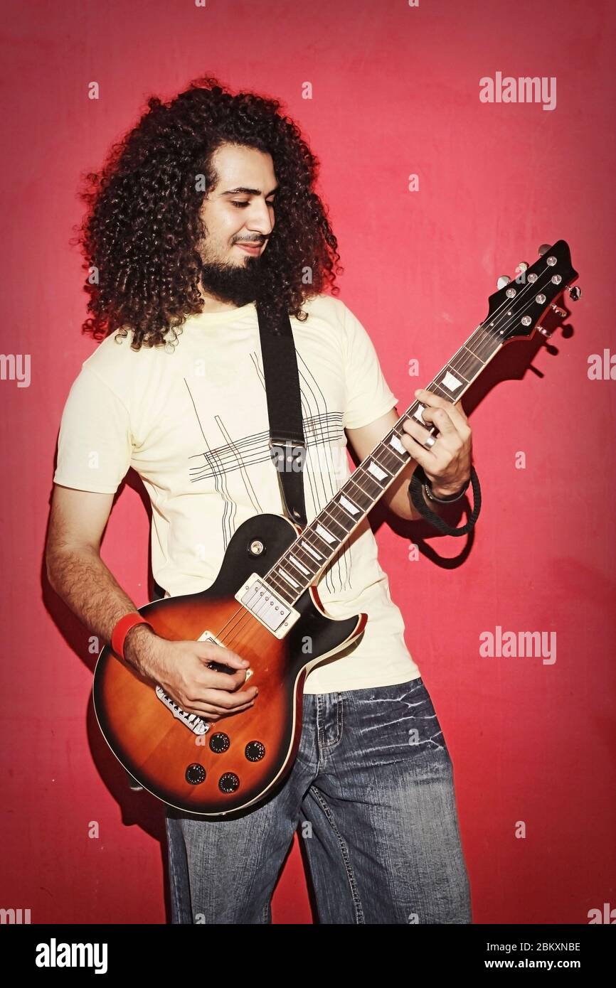Closeup of one handsome passionate expressive cool young brunette rock musician men with long curly hair playing electric guitar standing Stock Photo