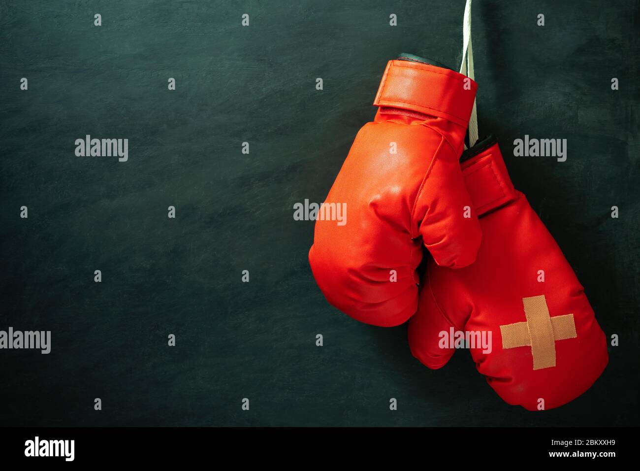 Red boxing gloves hung on black cement wall in darkness with lighting