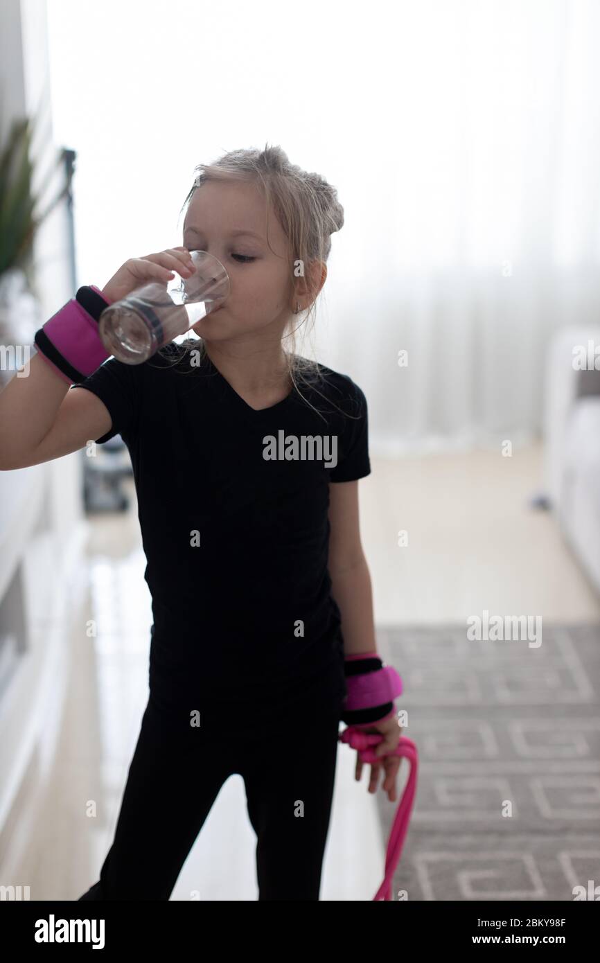 Little girl in a black bathing suit drinking water after hard physical exercises Stock Photo