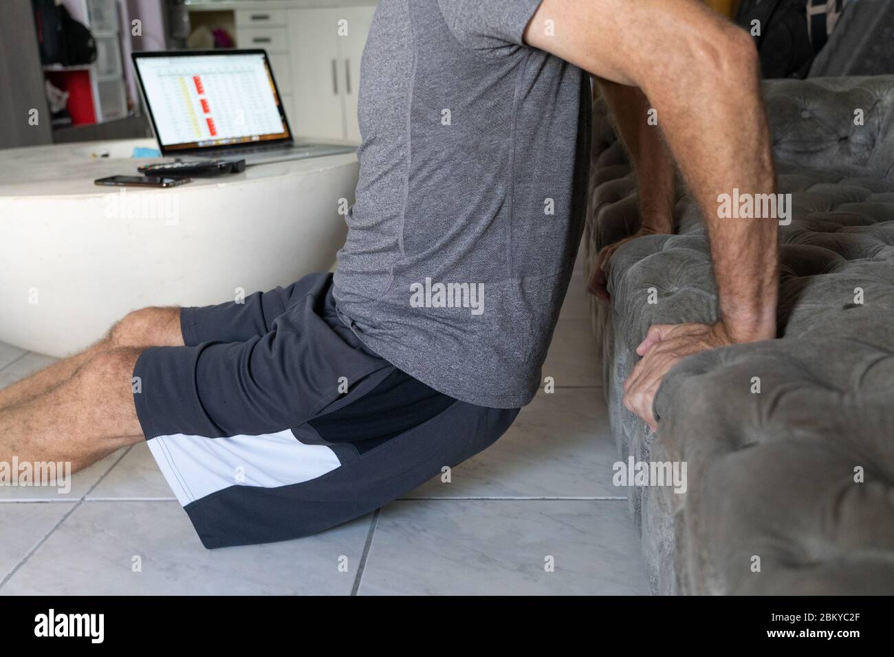 A man undertaking physical fitness exercise within an apartment during the COVID-19 Pandemic 2020.A computer in the background with the screen highlighting International infection rates and deaths from the Pandemic. Stock Photo
