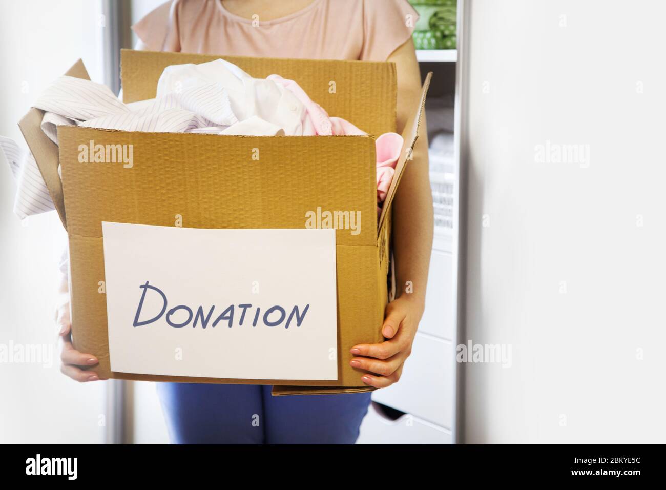 A girl stands near the wardrobe and holds a box with things. Clothes for donation. Stock Photo