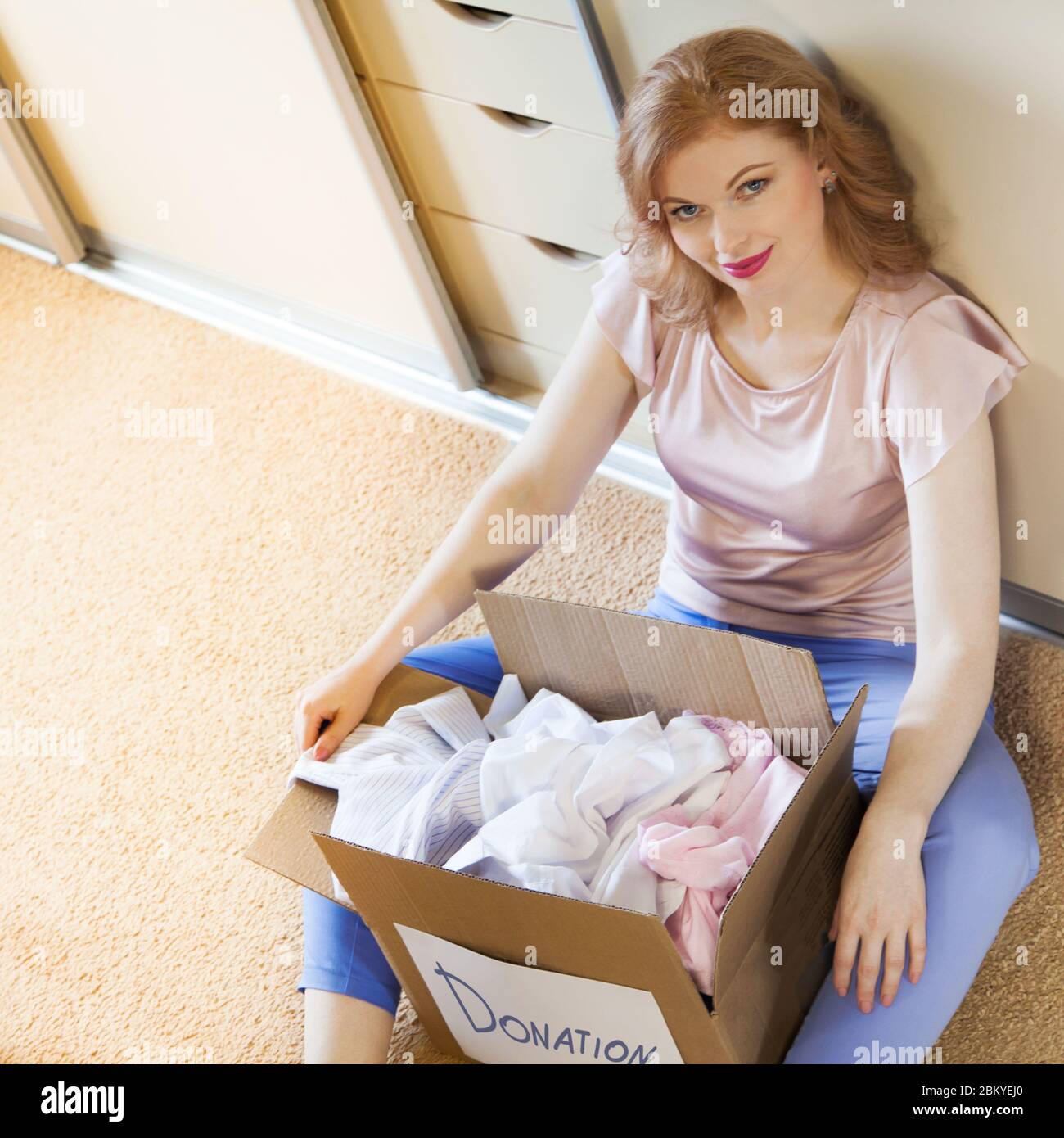 A girl sitting near the wardrobe and holds a box with things. Clothes
