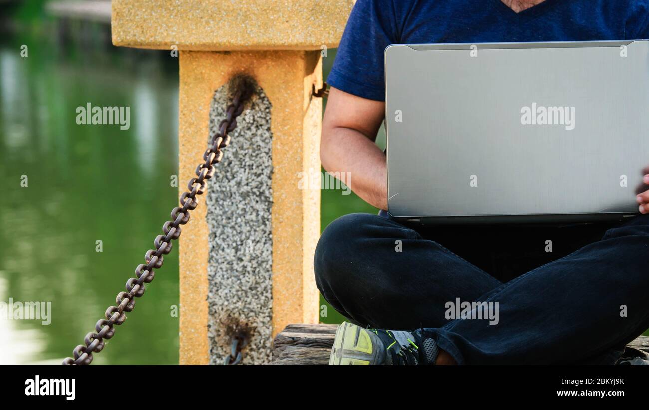 A man were blue shirt who working remotely by using laptop computer in the park. Stock Photo