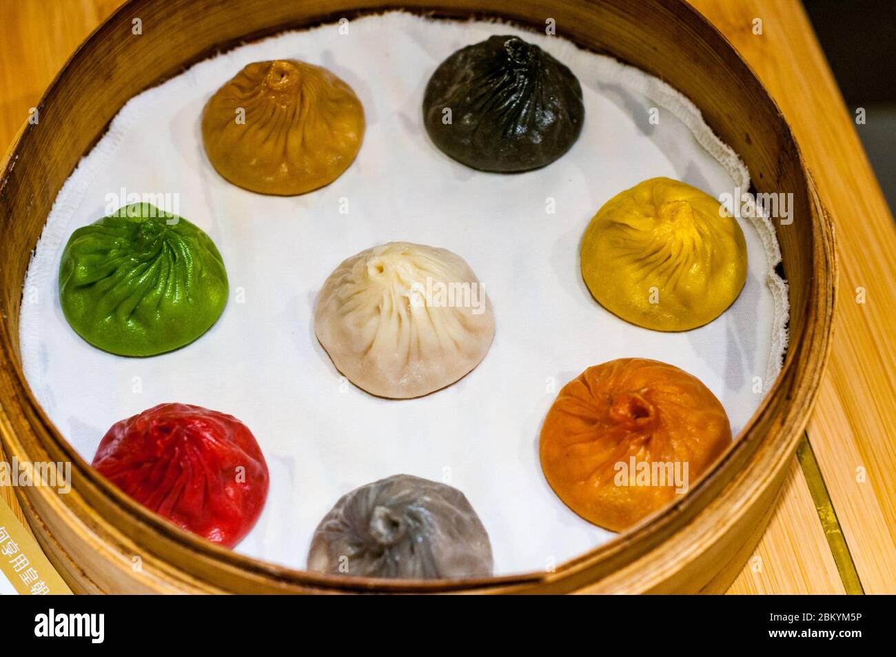 A bamboo steamer basket full of colorful xiaolongbao soup dumplings at