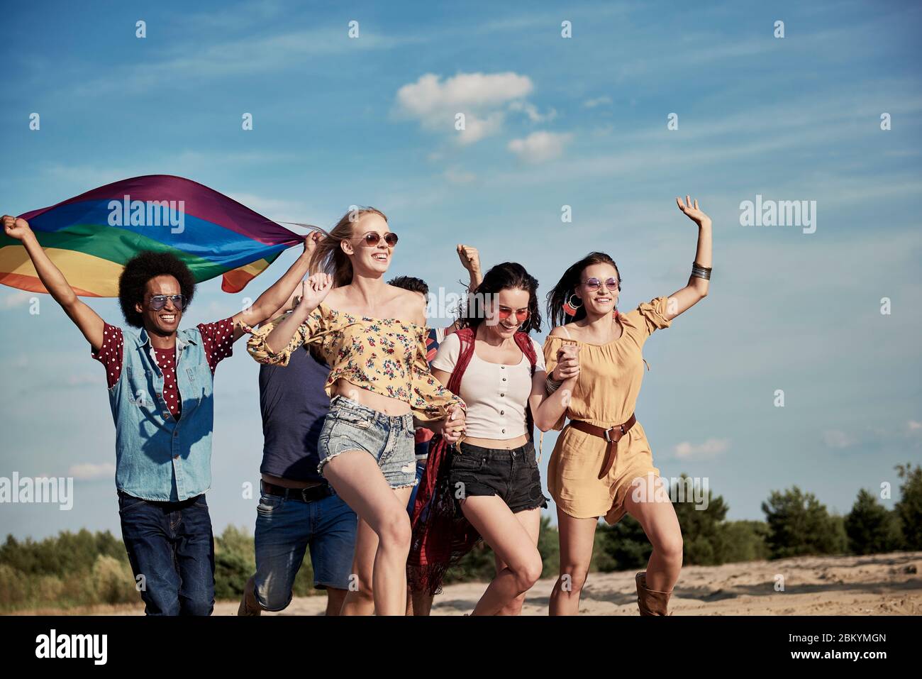 Happy friends with rainbow flag running outdoors Stock Photo