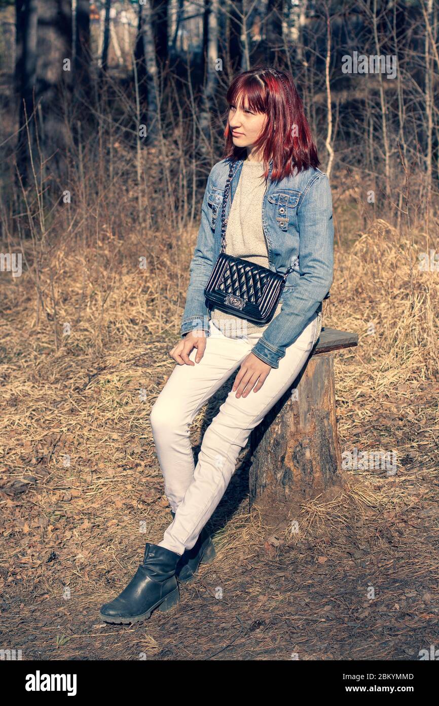 A young red-haired girl sits on a stump in the forest. European ...