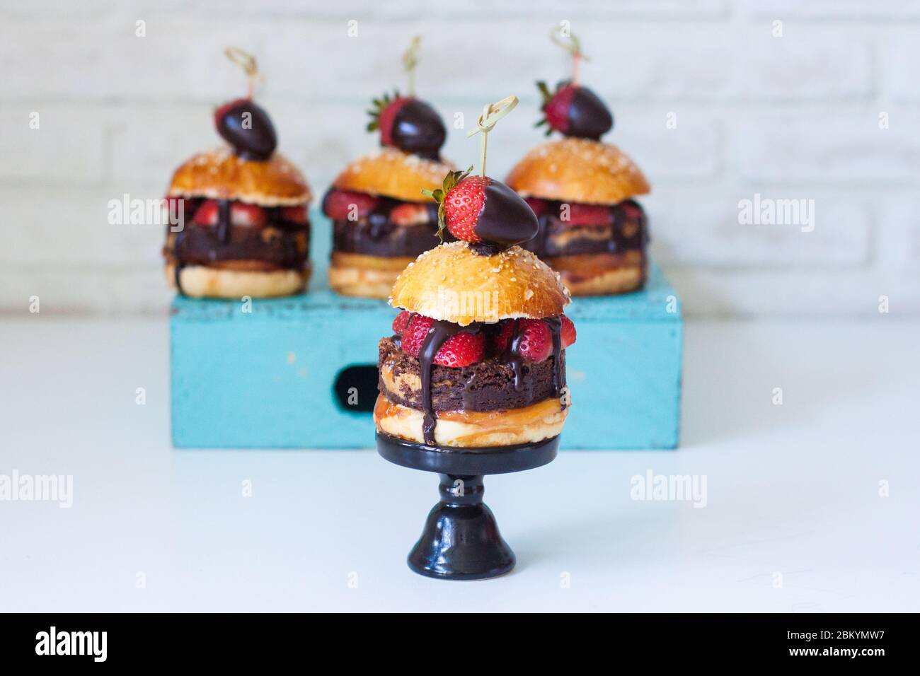 Sweet burger with vanilla bun, brownie layer, strawberries in chocolate and salted caramel. Stock Photo