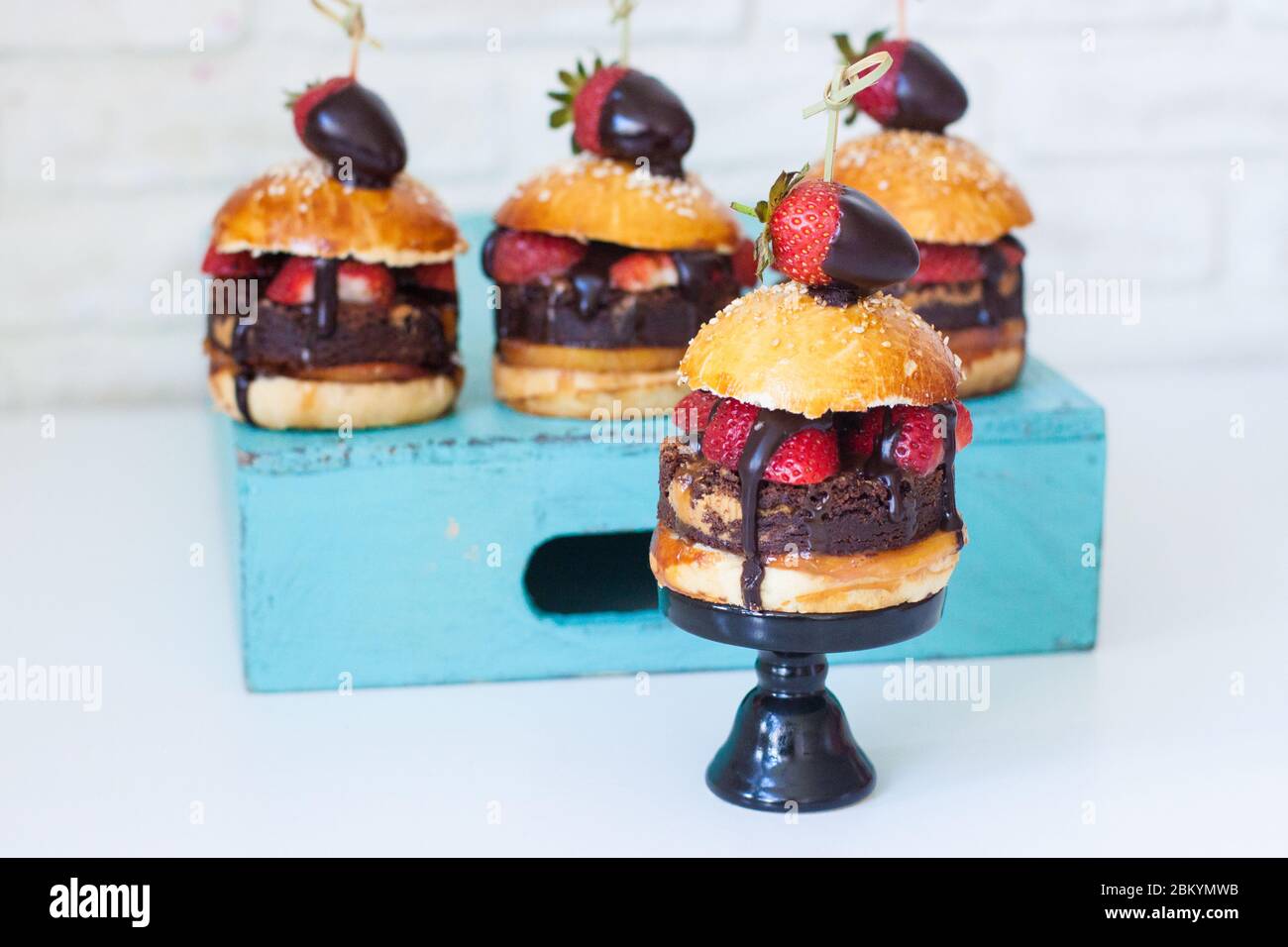Sweet burger with vanilla bun, brownie layer, strawberries in chocolate and salted caramel. Stock Photo