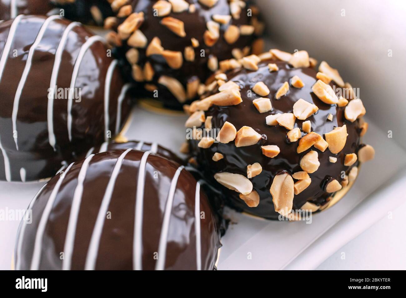 Chocolate covered Bavarian cream donut topping with crush peanuts in paper box. Tasty dessert pastry. Stock Photo