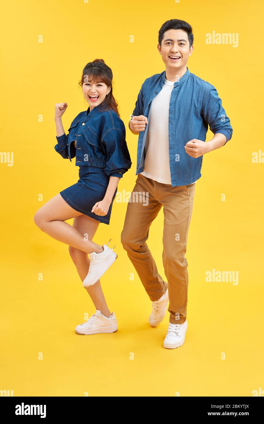 Portrait of funky couple jumping in air holding hands up enjoying time together isolated on yellow background Stock Photo