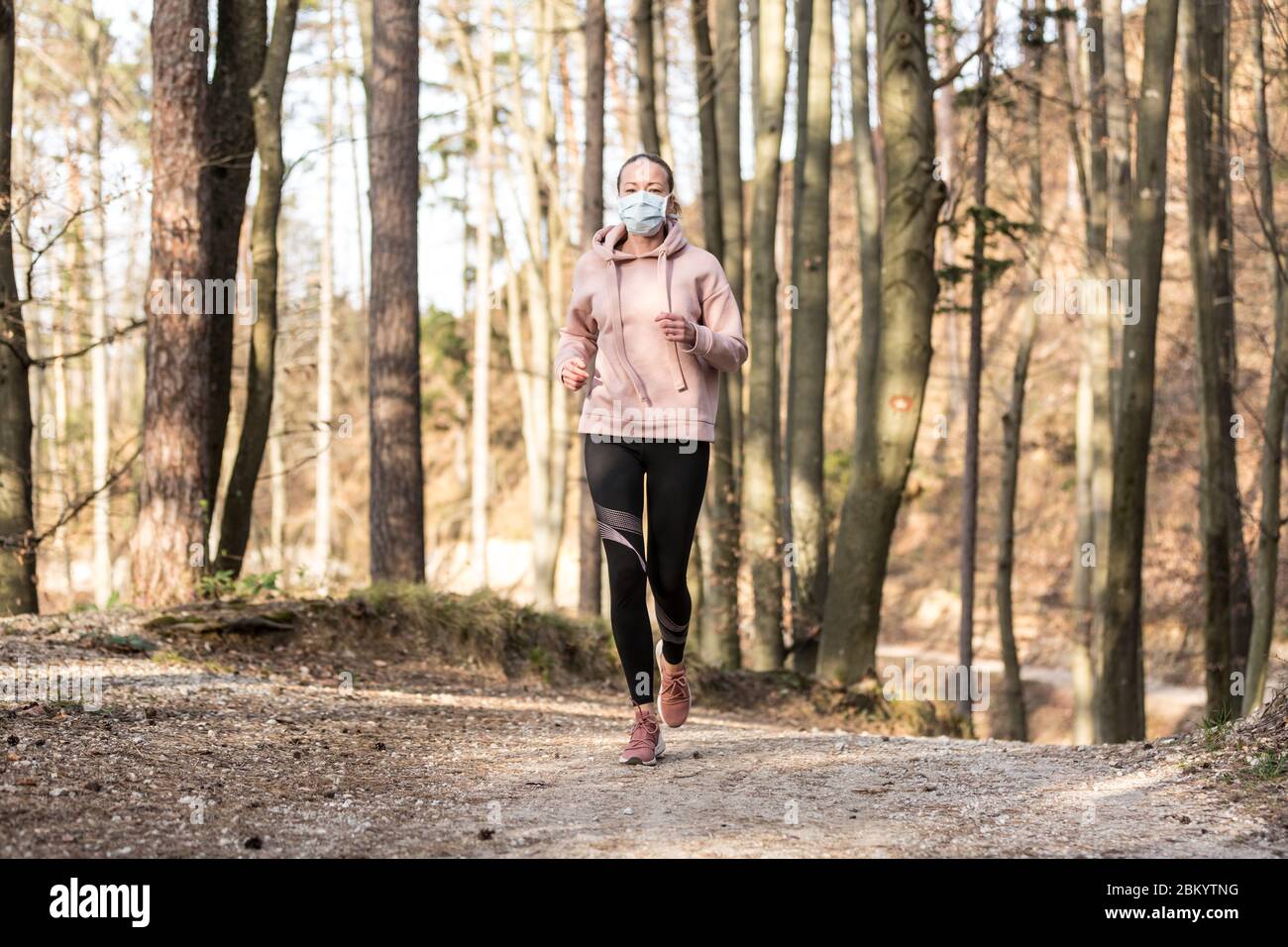 Corona virus, or Covid-19, is spreading all over the world. Portrait of caucasian sporty woman wearing a medical protection face mask while running in Stock Photo