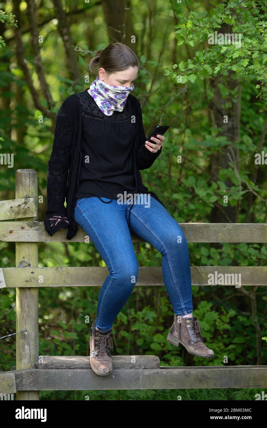 Young Women sitting on a wooden fence reading text message on a mobile phone. Stock Photo