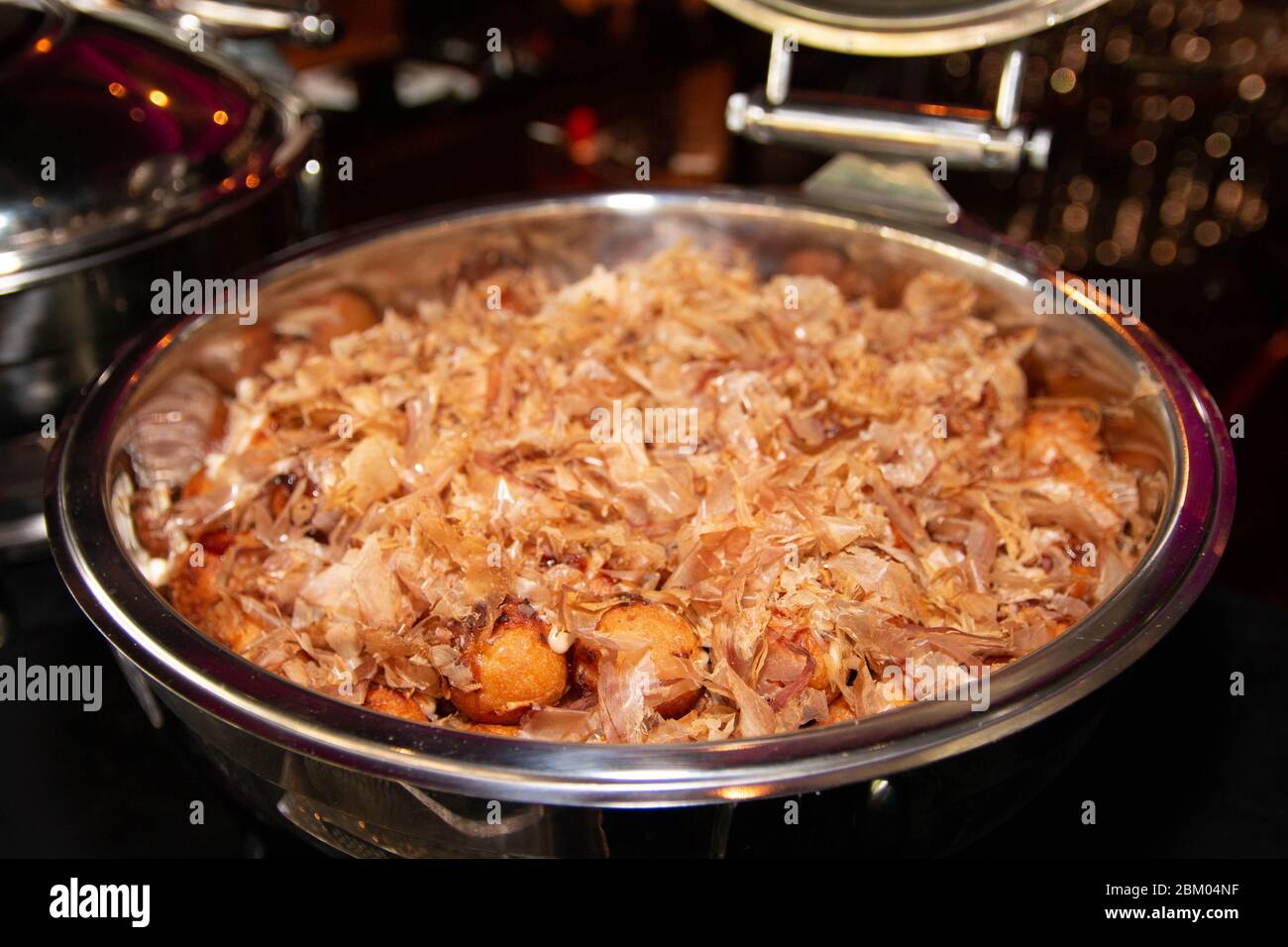 Large portion of Japanese style Takoyaki with dried bonito flakes on top in a buffet tray. Stock Photo