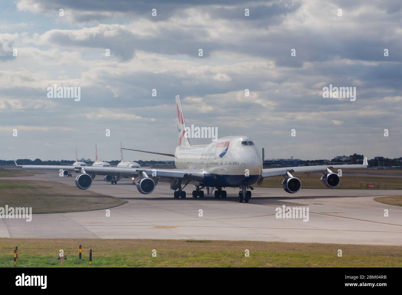 A Boing 747 airliner (Jumbo jet) belonging to British Airways lines up on a taxi-way with other airliners at Heathrow Airport, London, UK Stock Photo