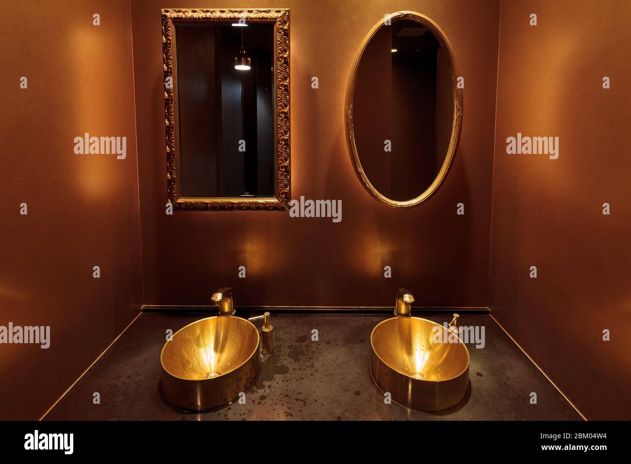A rectangular and oval mirror  above gold-coloured sinks  in a toilet in a restaurant in Tokyo, Japan. Stock Photo