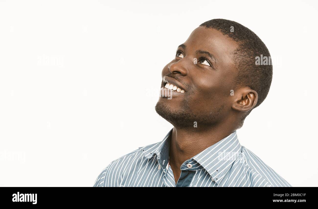 African american handsome man toothy smiles looking up and to the side, Dark-skinned young guy in blue striped shirt isolated on white background Stock Photo