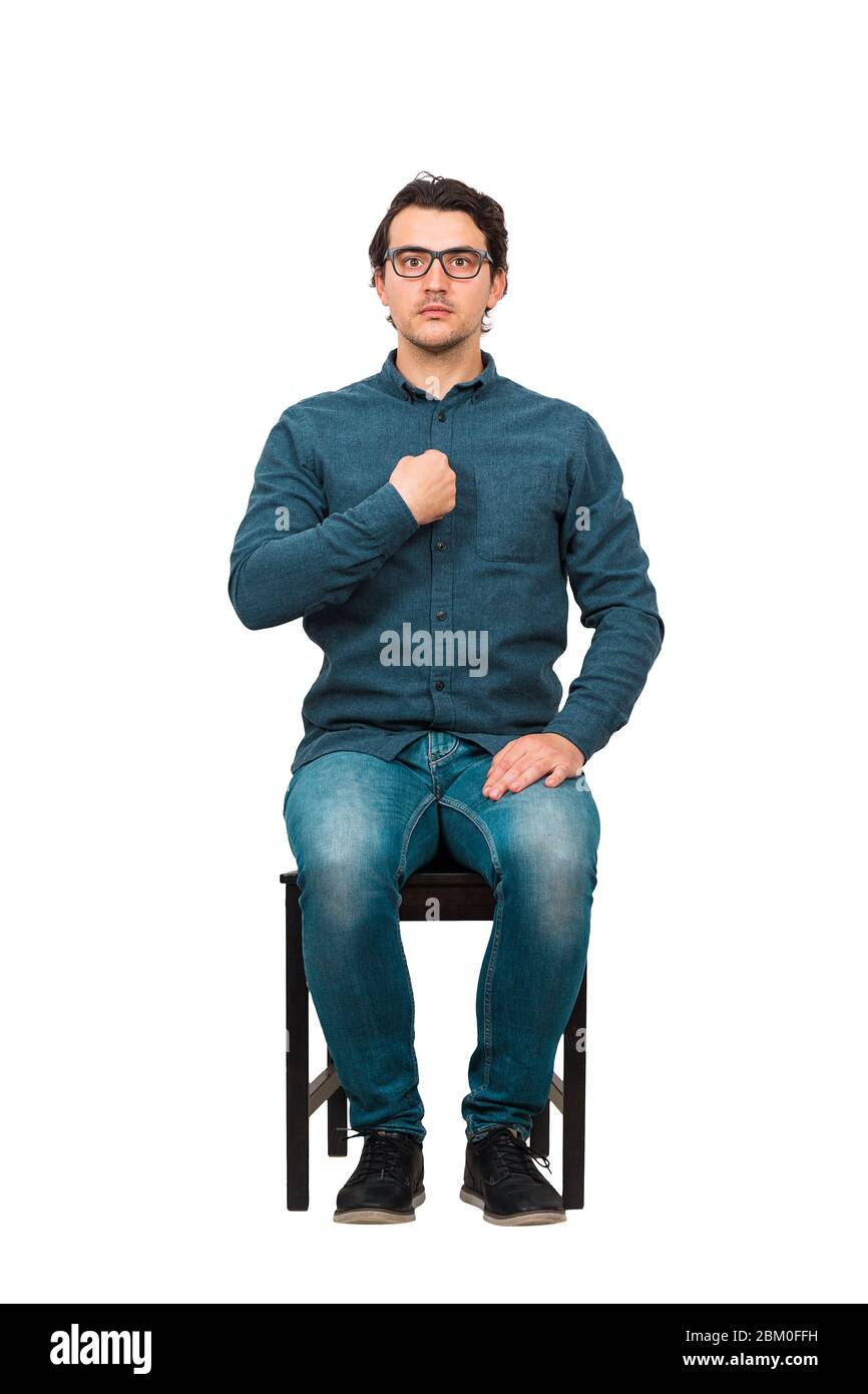 Full length portrait of perplexed businessman, seated on a chair points index finger to himself, looking confused to camera isolated on white backgro Stock Photo