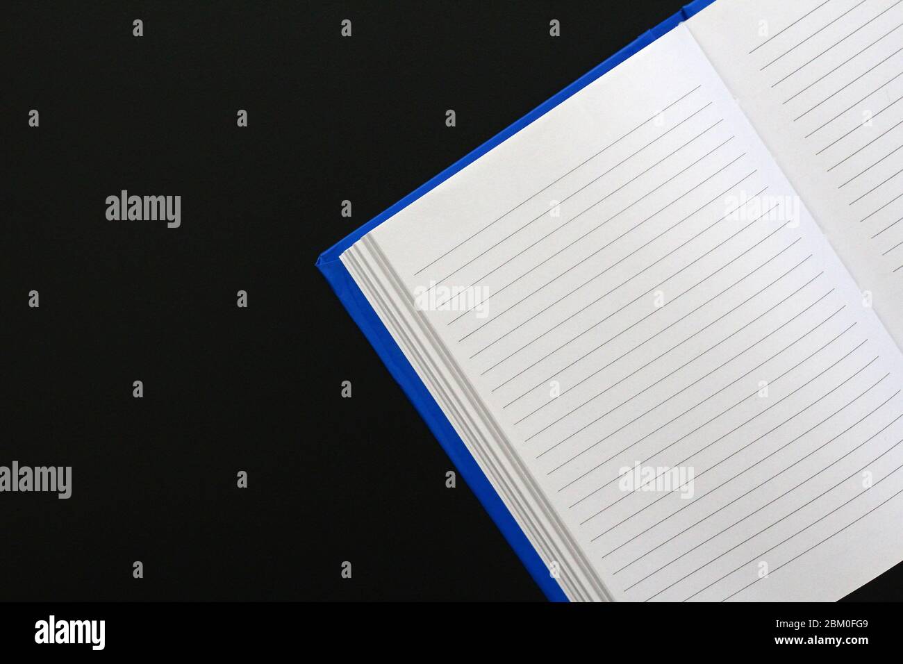 Blue notebook with text lines on white paper, on a not totally black metallic surface. A lot of copy space. (Suggestion: do a horizontal mirror flip t Stock Photo