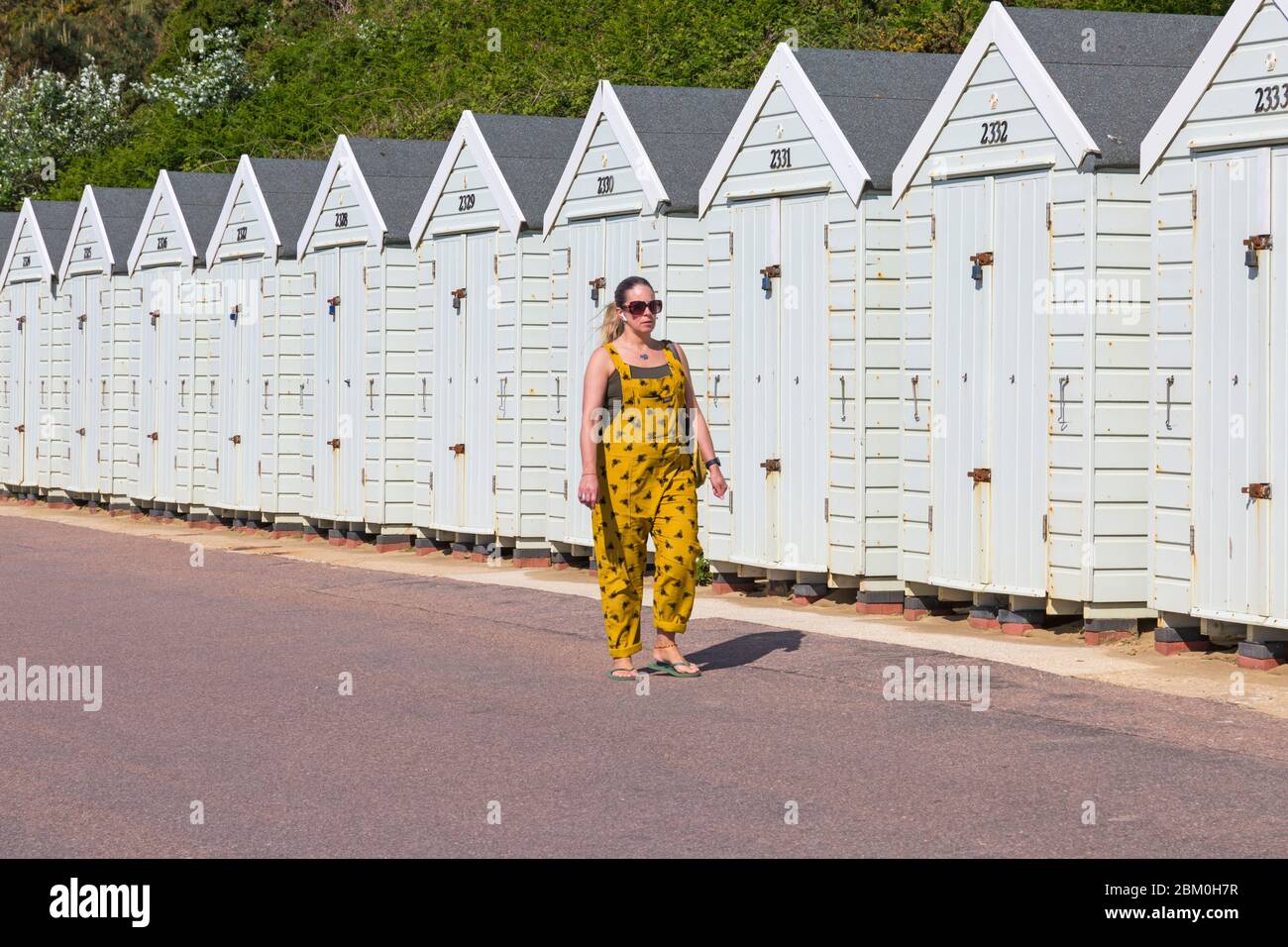 Bournemouth, Dorset UK. 6th May 2020. UK weather: lovely warm sunny day with temperatures rising ready for the long bank holiday weekend.  Beaches are mainly deserted with people taking their permitted exercise at the seaside, most adhering to the Coronavirus guidelines.  Woman walking along promenade past beach huts. Credit: Carolyn Jenkins/Alamy Live News Stock Photo