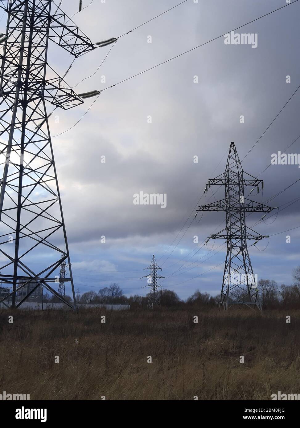 Metal pylons of a power line against a disturbing cloudy sky on the outskirts of a city. High voltage towers. Desolate landscape. Apocalypse concept Stock Photo