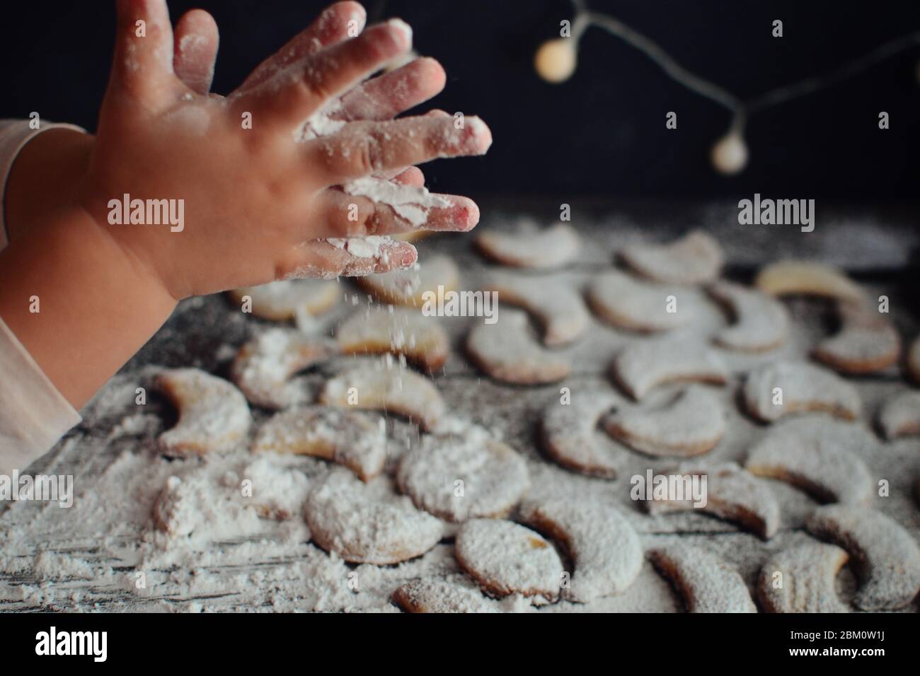 A child sprinkles powdered sugar cookies. Children's hands and flour. Baby is preparing Christmas cookies. Cute baby hands. Baby and cookies. Stock Photo