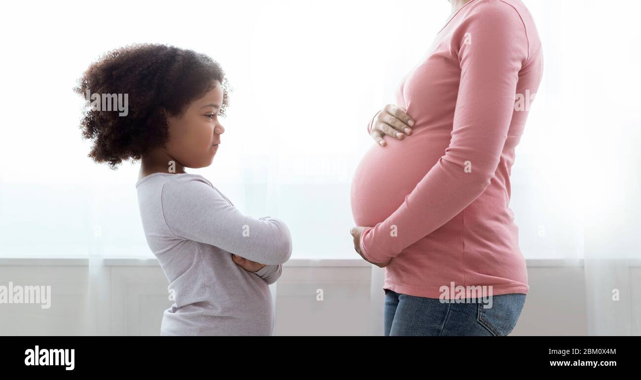 Little Black Girl Looking At Her Pregnant Mom's Belly With Jealousy Stock Photo