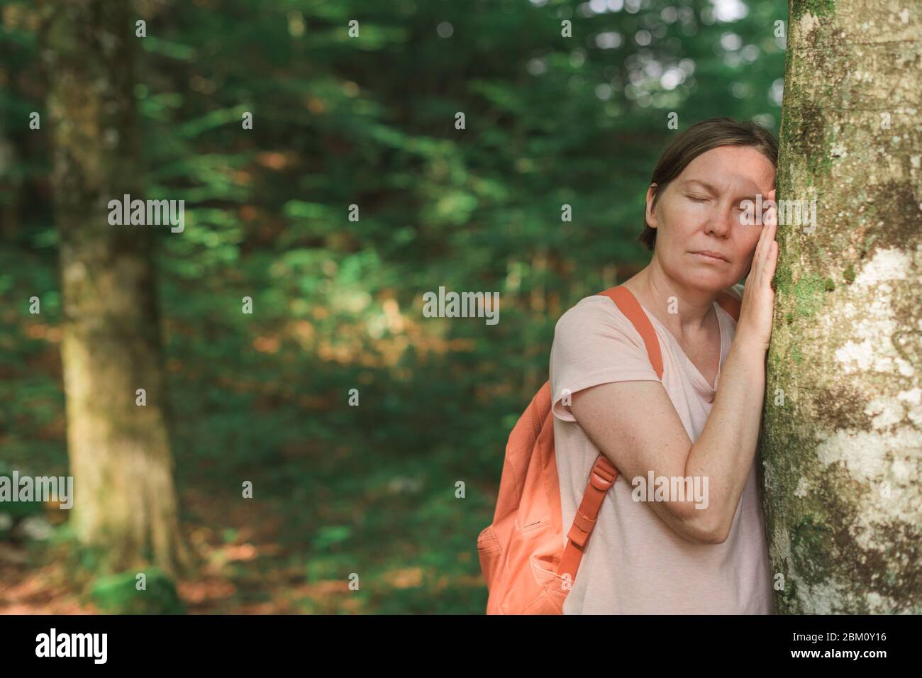 Female environmentalist leaning on tree trunk in forest, selective focus Stock Photo