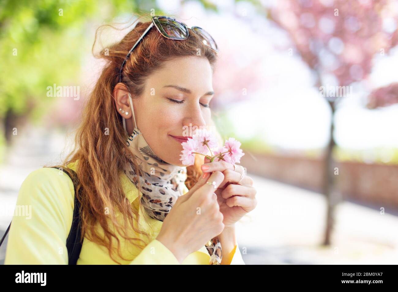 Young redhead woman smelling cherry blossom in park during Sakura Stock Photo