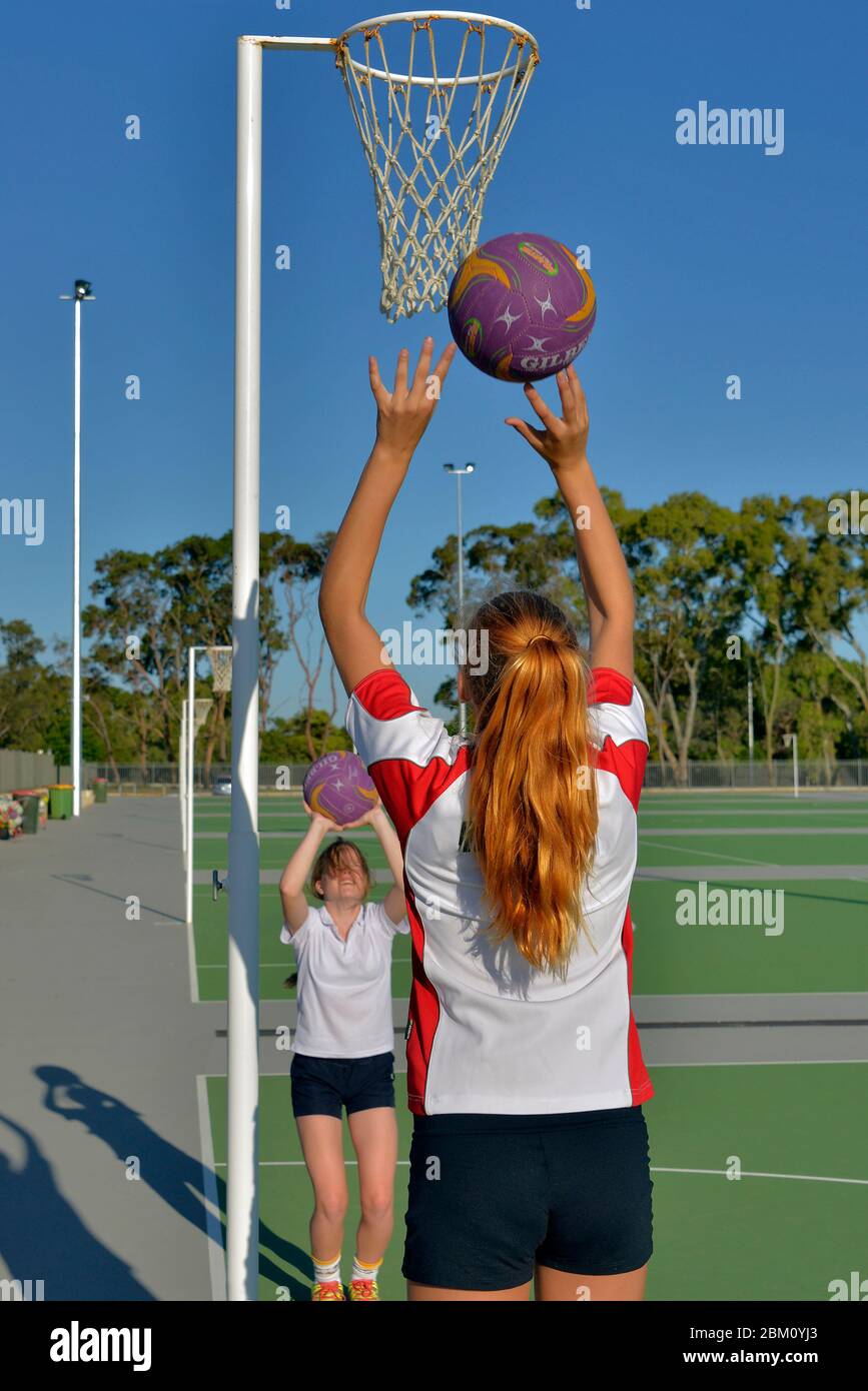 A portrait format, rear view of a girl throwing a basketball into a net