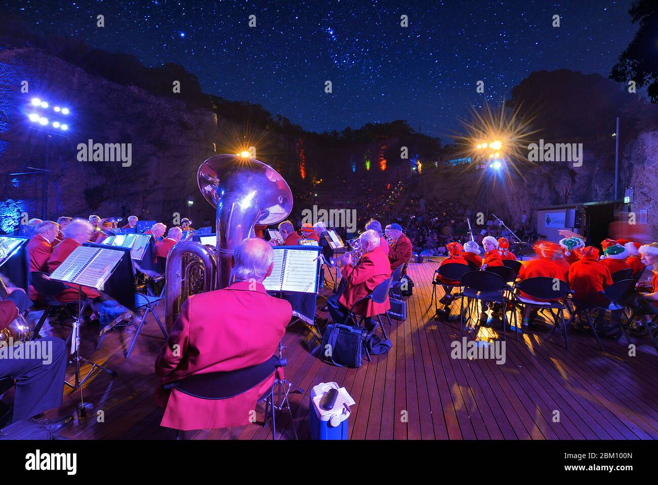 A brass band playing a concert at an outdoor amphitheatre under the stars. Point of view is from the back of the stage looking towards the audience. Stock Photo