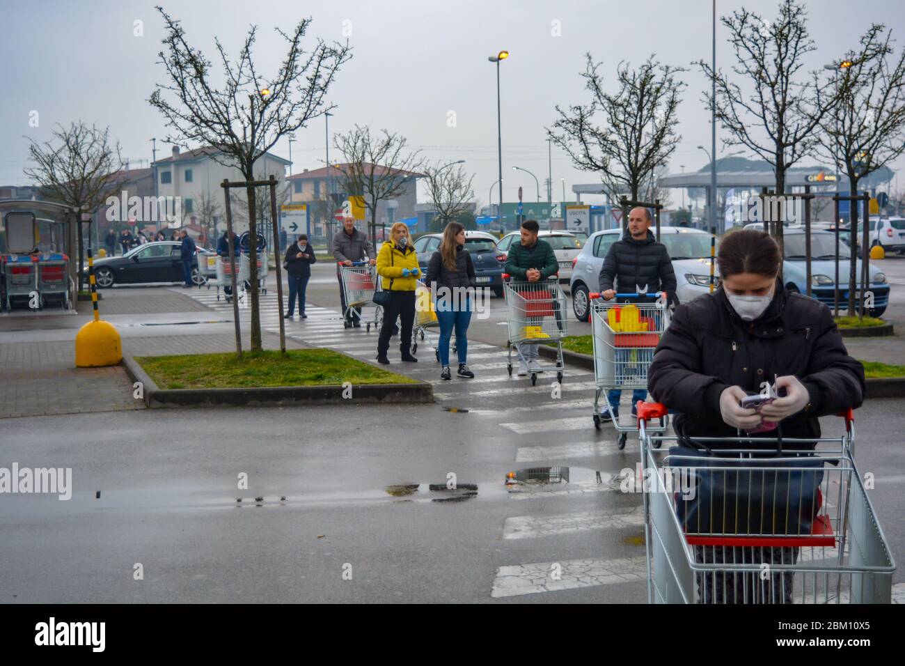 Closeup of italian woman with mask and gloves standing with her shopping cart in a long line to stock up groceries. Social distancing for coronavirus Stock Photo