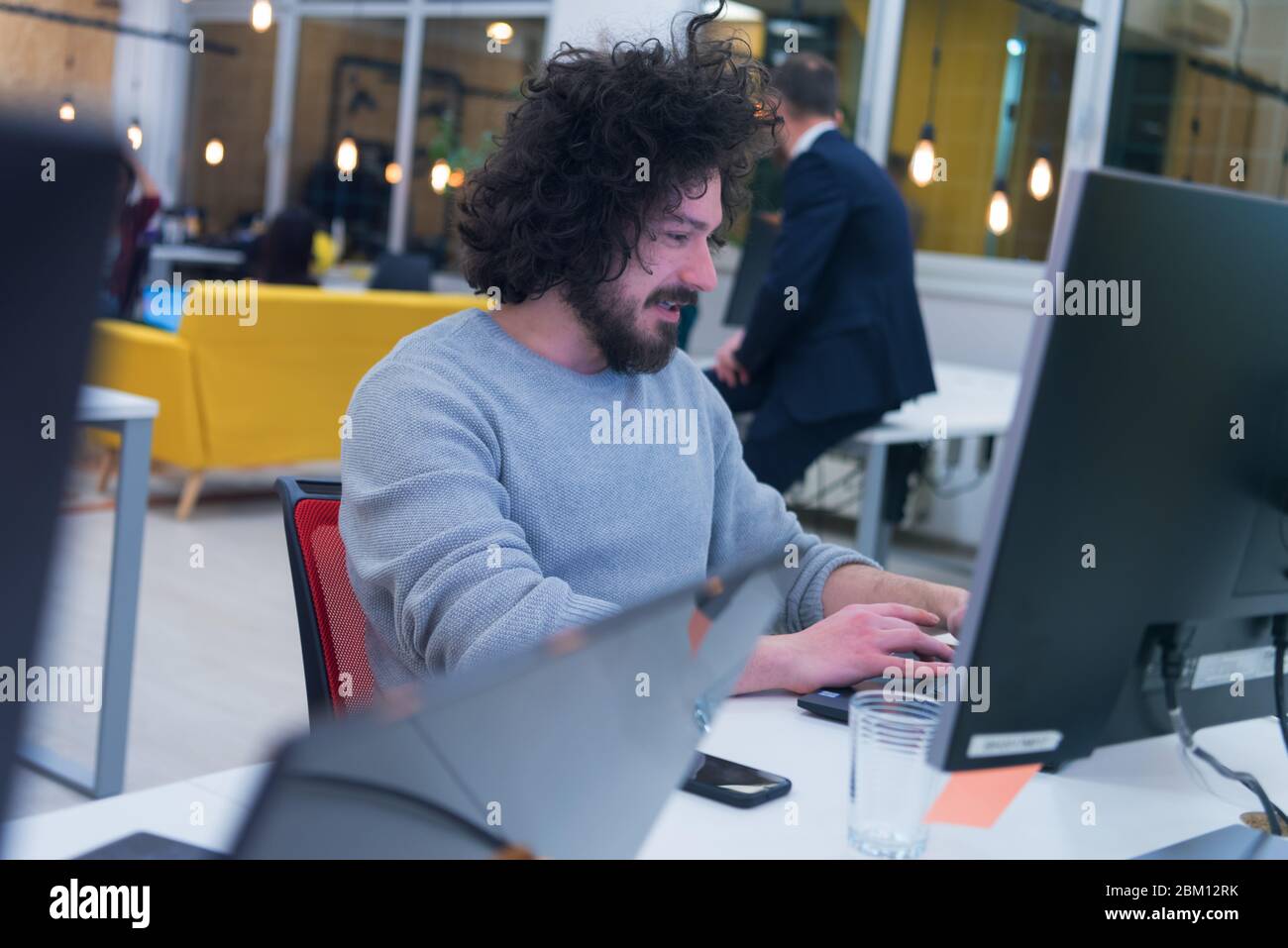 Young man working on his computer in co-creative space.  Working on new creative digital projects inside modern co working space. Stock Photo