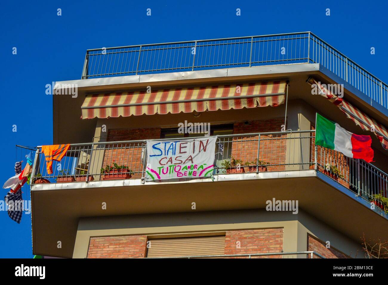 Positive message on a banner from balcony 'Stay home, everything is gonna be alright',the italian flag waving and hanging clothes.Encouragement text Stock Photo