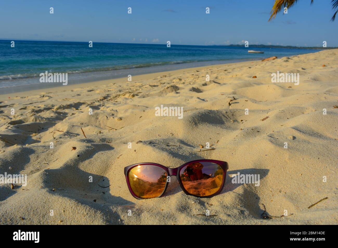 Fantastic tropical holiday scene: a pair of sunglesses on a sunny beach, over fine golden sand, in the back crystal clear blue ocean and clean horizon Stock Photo