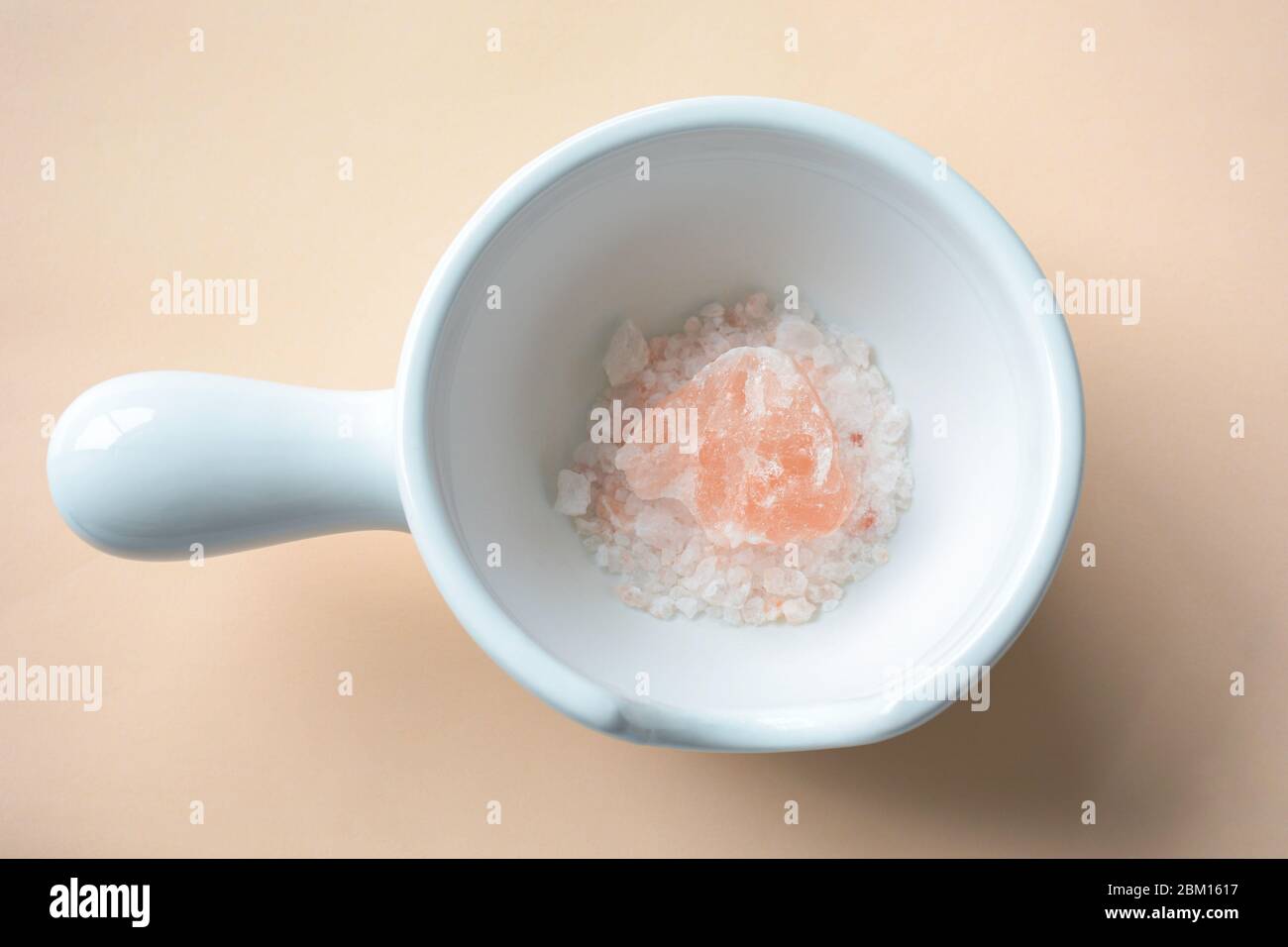 Himalayan pink rock salt crystals pieces in a ceramic white bowl mortar on coral background Stock Photo