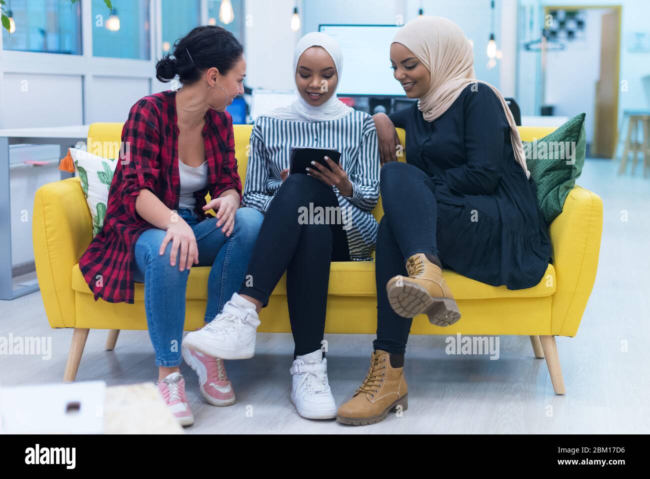 Diverse group of multiethnic young businesswomen working as a team. Two Muslim hijab and one american female co workers discussing important issues si Stock Photo