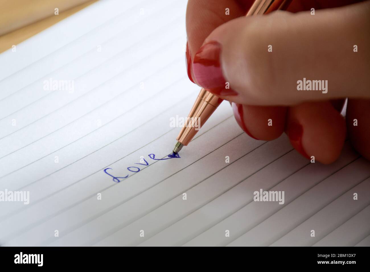 Close up manicured female hand writes the word love in notebook. Valentine's day and love concept. Stock Photo