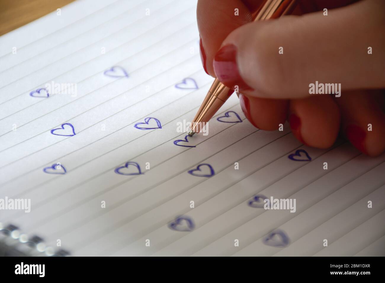 Manicured female hand draws many hearts in notebook. Valentine's day and love concept. Stock Photo